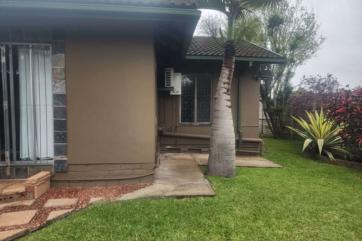 A view of the rear exterior of the house featuring a concrete pathway, landscaped garden, and mounted air conditioning unit.