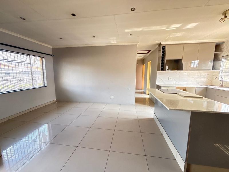 An open-plan living and kitchen area featuring modern cabinetry, stone countertops, a central island, and neutral tiled flooring throughout.