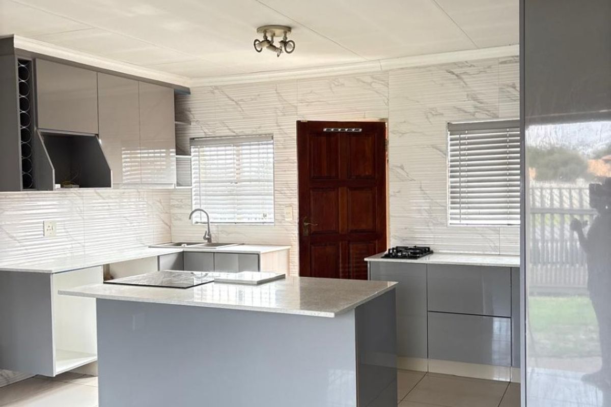 Modern kitchen featuring grey high-gloss cabinetry, stone countertops, a central island, gas hob, and marble-look wall tiles with neutral tiled flooring.