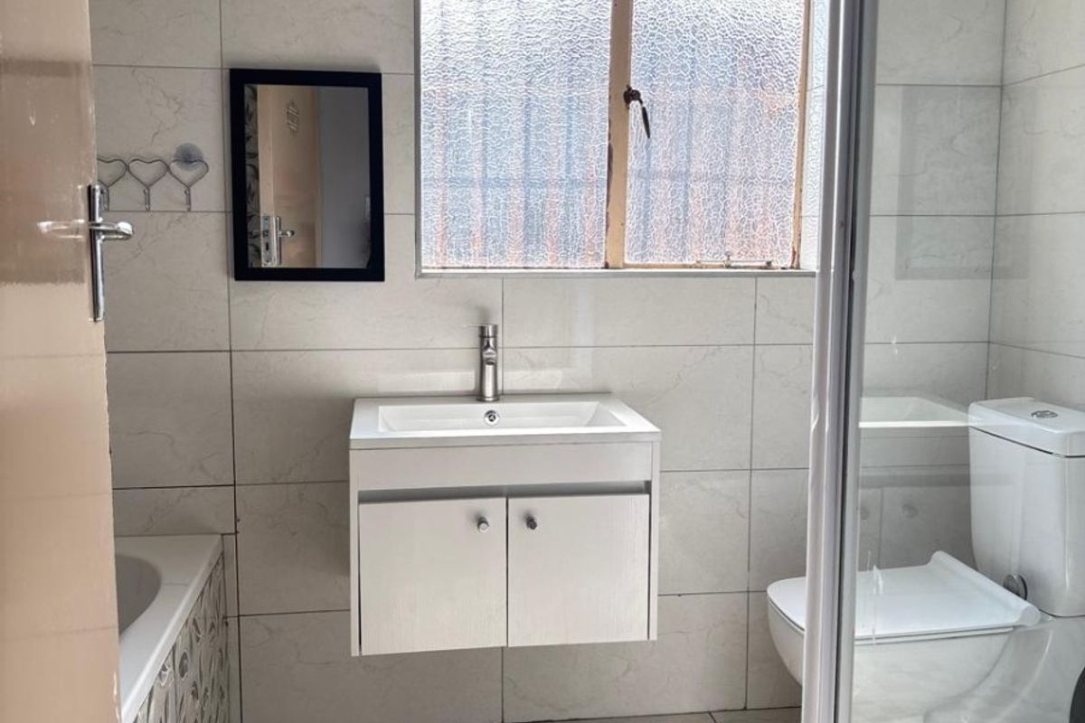 A clean, modern bathroom featuring a wall-mounted vanity, a separate shower enclosure, a bathtub, and neutral floor-to-ceiling tiling.