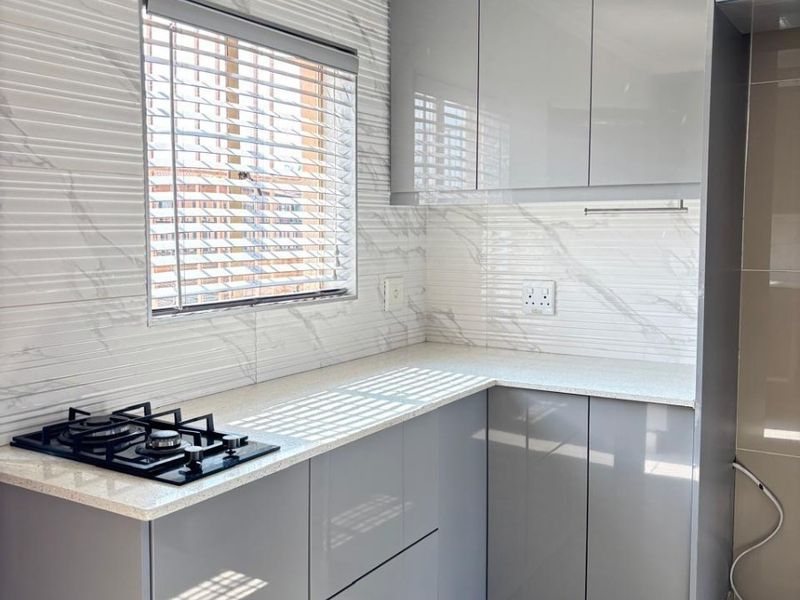 Modern kitchen featuring sleek grey cabinetry, stone countertops, a built-in gas hob, and stylish marble-effect tiled backsplash.