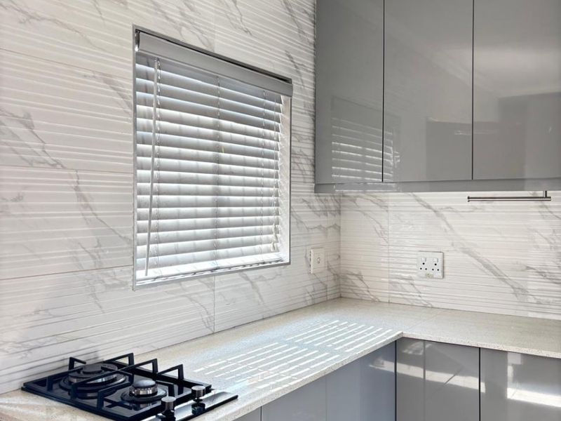 Modern kitchen featuring sleek grey cabinetry, stone countertops, a built-in gas hob, and stylish marble-effect wall tiling.
