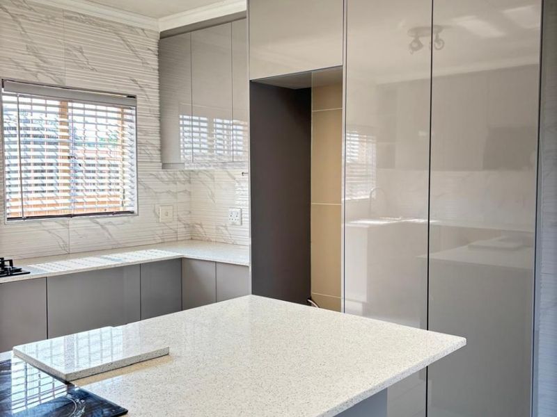 Modern kitchen featuring high-gloss cabinetry, quartz countertops, a central island with an integrated hob, and stylish marble-look tile backsplash.