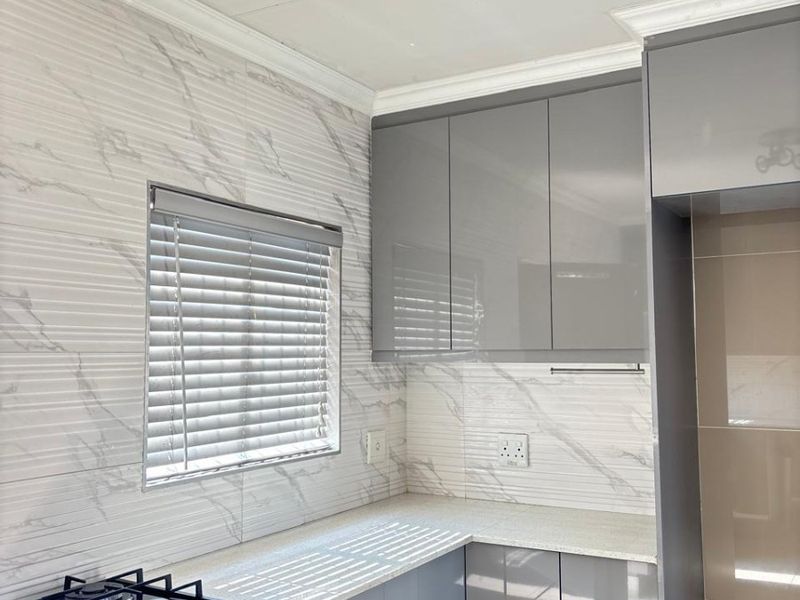 Modern kitchen featuring sleek grey cabinetry, stone countertops, marble-effect wall tiling, and a built-in gas hob.