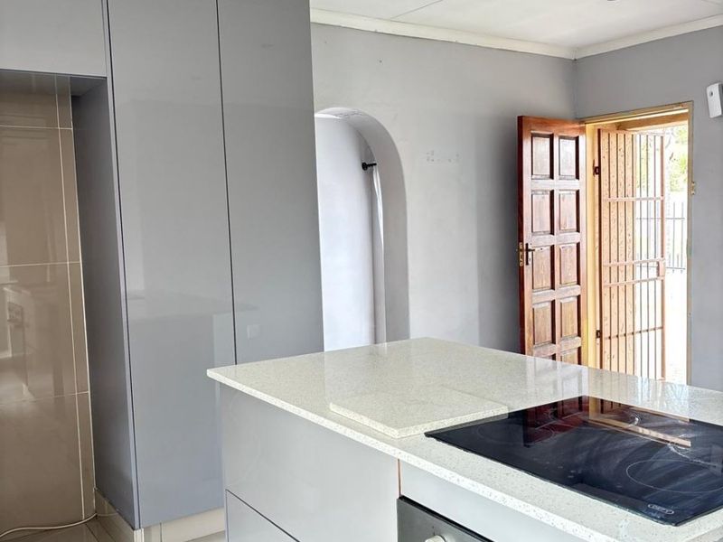 Modern kitchen featuring a central island with a built-in oven and electric cooktop, sleek grey cabinetry, and tiled flooring.