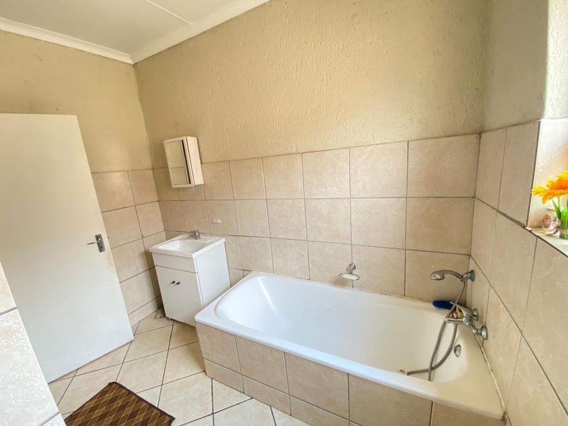 A functional bathroom featuring a built-in bathtub, vanity cabinet, and neutral ceramic tiling throughout.