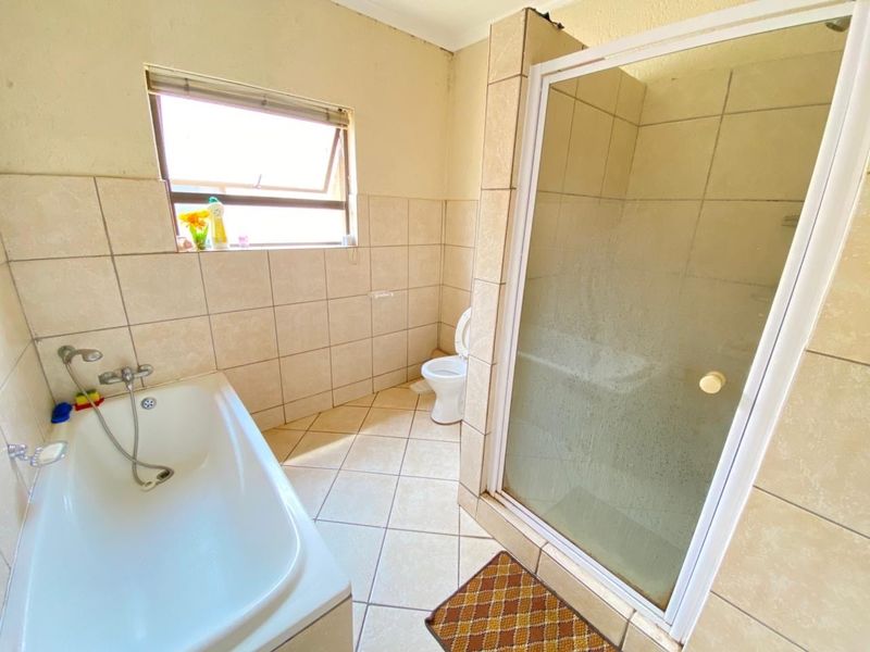 A functional bathroom featuring a bathtub, separate shower enclosure, and toilet with neutral wall and floor tiling.