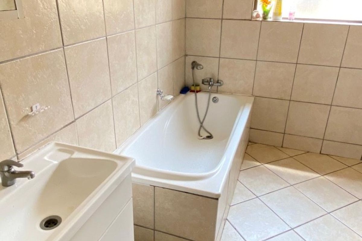 A functional bathroom featuring a built-in bathtub with handheld shower, a vanity cabinet, and neutral ceramic tiling throughout.