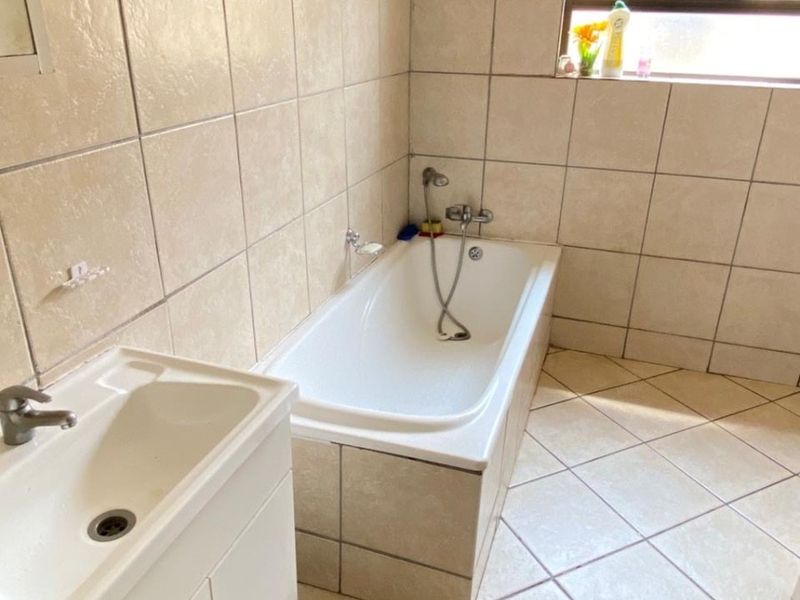 A functional bathroom featuring a built-in bathtub with handheld shower, a vanity cabinet, and neutral ceramic tiling throughout.