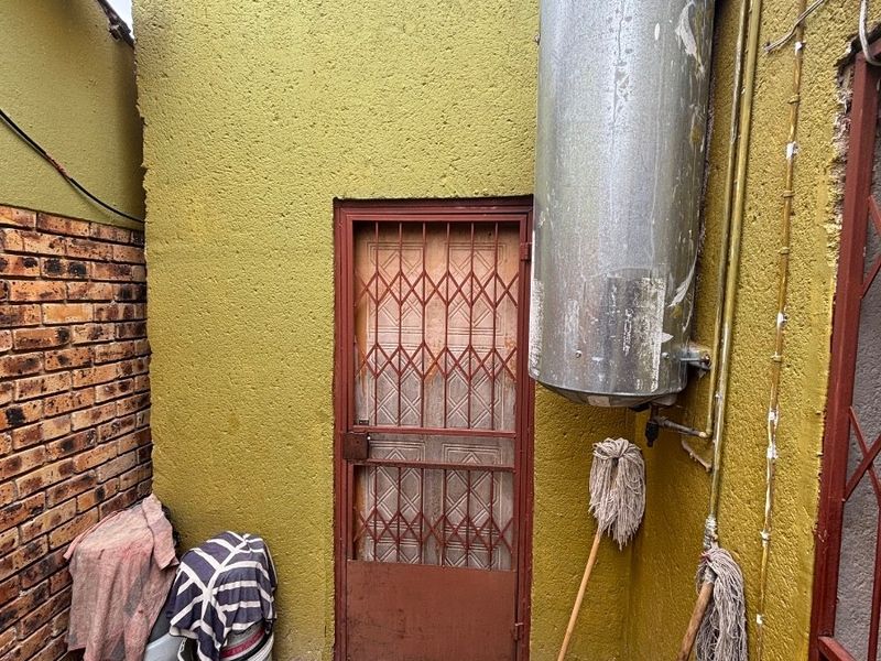 A small exterior utility area featuring a wall-mounted electric water heater, a security gate, and exposed brickwork.