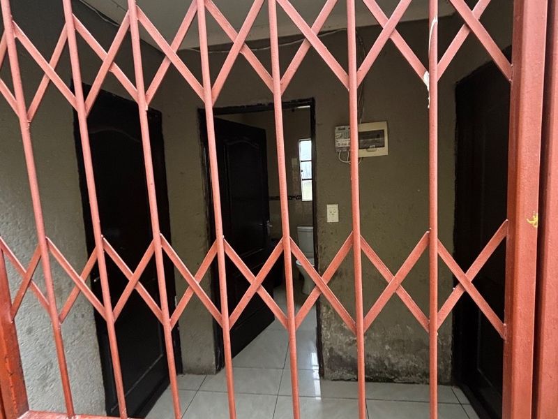 An entrance area featuring a security gate, tiled flooring, and visible wall surface wear, leading into the interior of the property.