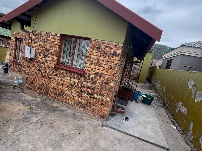 Rear view of a face brick house featuring a concrete apron and a boundary wall with visible weathering and paint deterioration.