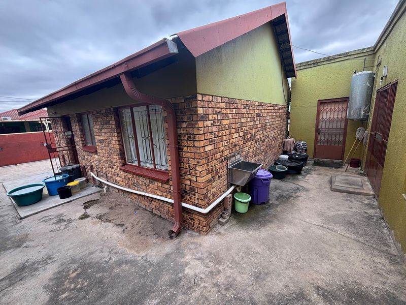 Rear exterior view of the property featuring face brick walls, a metal roof, concrete paving, and an external utility sink area.