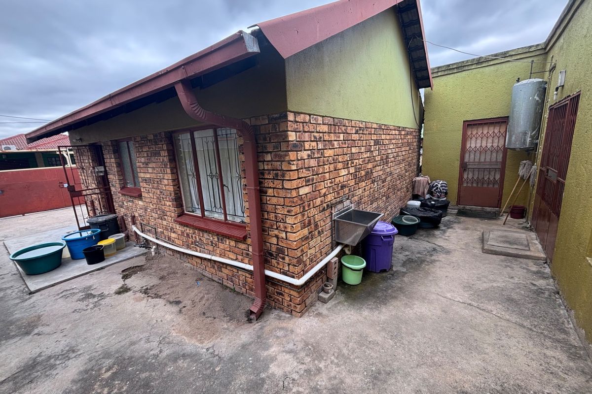 Rear exterior view of the property featuring face brick walls, a metal roof, concrete paving, and an external utility sink area.
