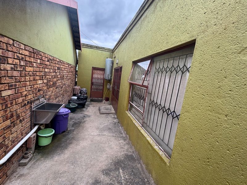 Side passage area featuring a stainless steel utility sink, security gates, and external geyser, with concrete paving and facebrick walling.