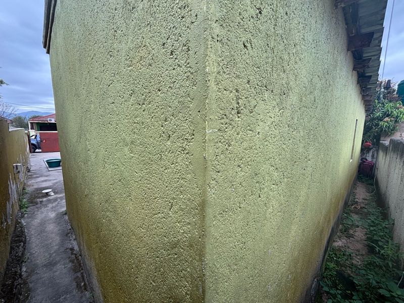 Side view of the property showing textured exterior walls with visible signs of weathering and organic growth at the base.