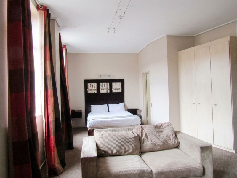 Spacious bedroom featuring built-in wardrobes, carpeted flooring, and track lighting, with a visible water stain on the ceiling.