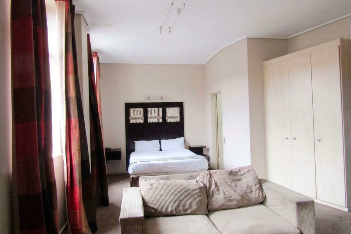 Spacious bedroom featuring built-in wardrobes, carpeted flooring, and track lighting, with a visible water stain on the ceiling.