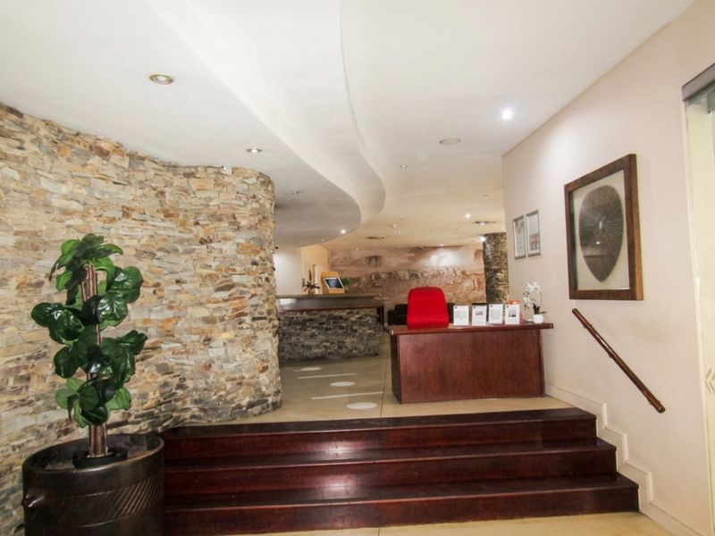 A welcoming entrance foyer featuring a striking stone feature wall, curved bulkhead ceiling with recessed lighting, and a timber staircase.
