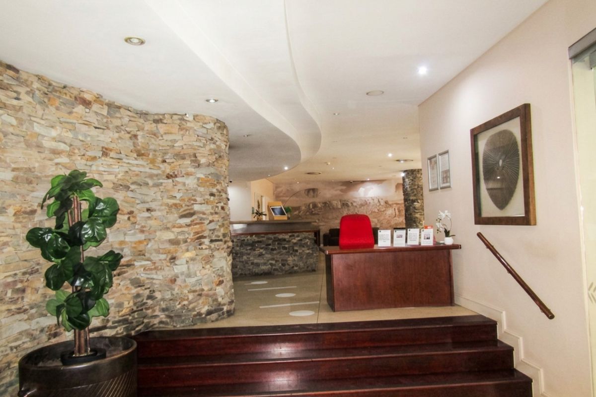 A welcoming entrance foyer featuring a striking stone feature wall, curved bulkhead ceiling with recessed lighting, and a timber staircase.