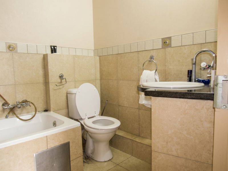 A functional bathroom featuring a built-in bathtub, toilet, and a vanity basin set into a granite countertop with neutral wall and floor tiling.