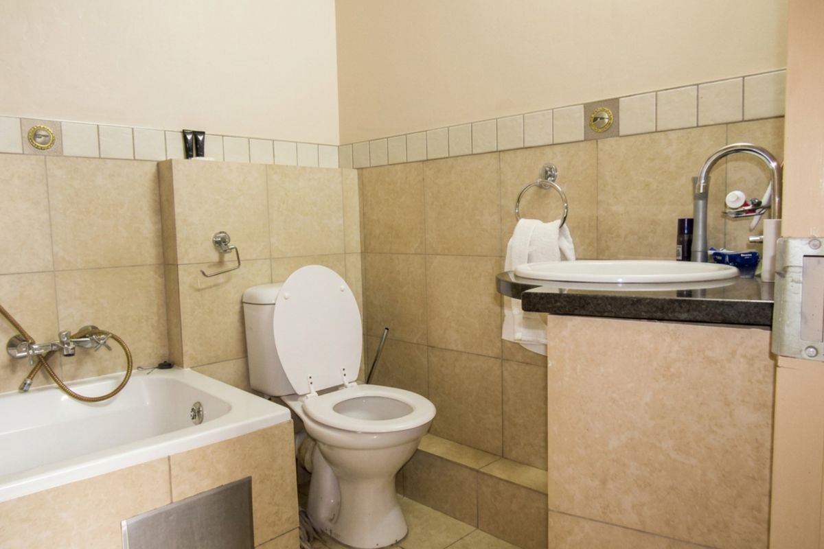 A functional bathroom featuring a built-in bathtub, toilet, and a vanity basin set into a granite countertop with neutral wall and floor tiling.