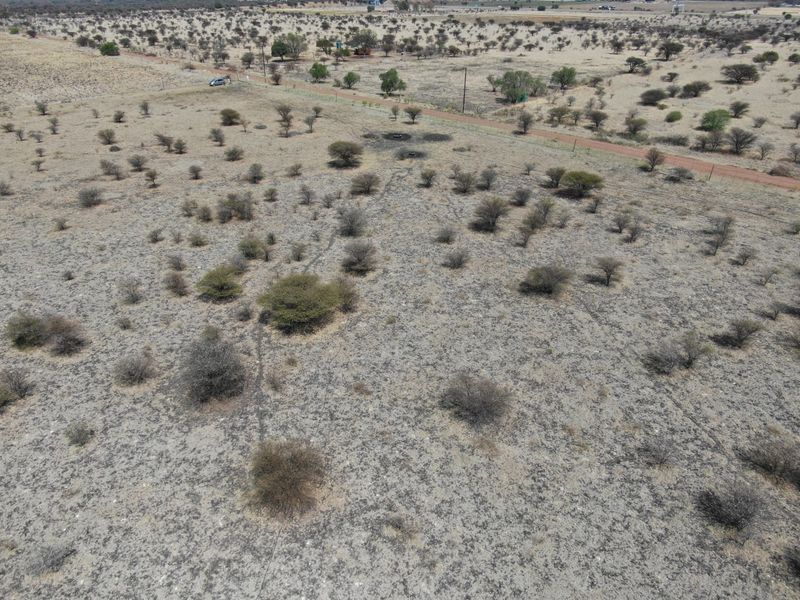 An aerial view of a large, undeveloped residential plot featuring natural vegetation, perimeter fencing, and access to a nearby dirt road.
