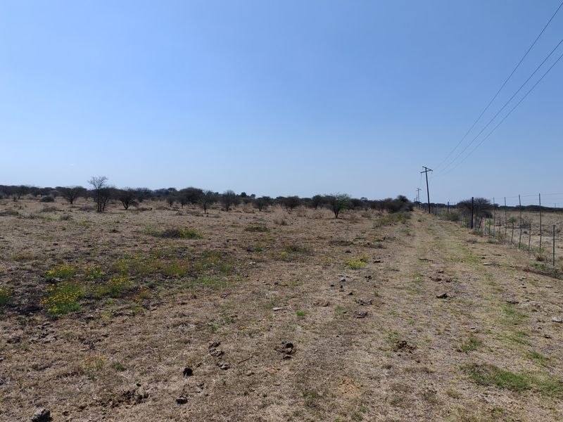 A view of a vacant residential plot featuring natural vegetation, wire perimeter fencing, and overhead utility lines.