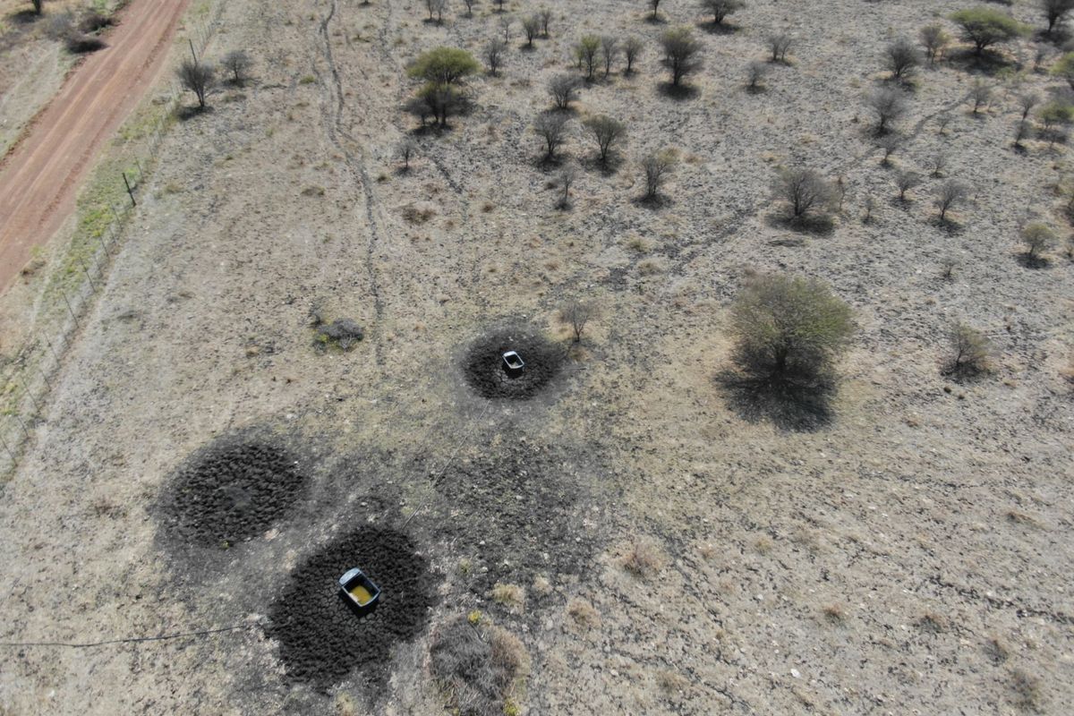 Aerial view of vacant residential land featuring a dirt access road, perimeter fencing, and established livestock water troughs in a natural bushveld setting.
