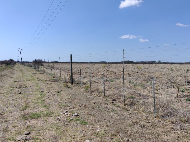 A view of a vacant residential plot featuring perimeter barbed wire fencing and overhead utility lines.