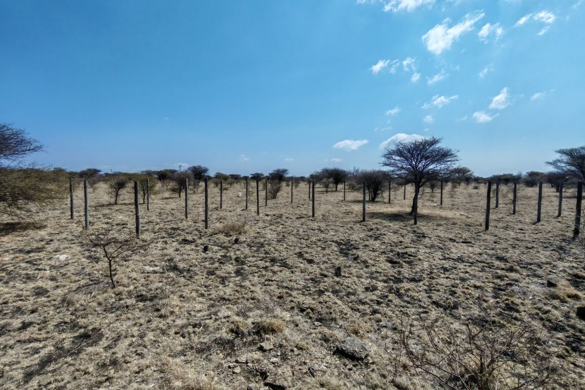 A view of a vacant residential plot featuring dry vegetation and existing fence posts across the landscape.