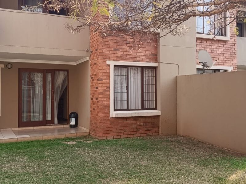 Rear view of an apartment building featuring a brick and plaster facade, a private tiled patio, and access to a shared garden area.