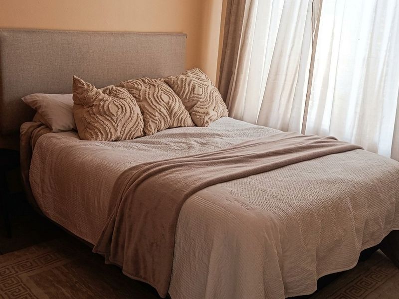 A cozy bedroom featuring neutral tones, natural light through curtains, and standard door hardware.