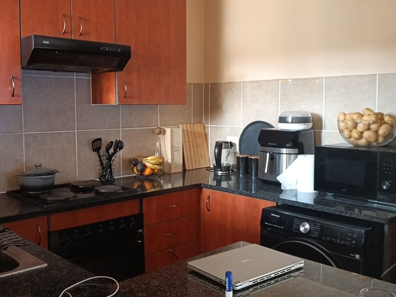 Functional kitchen featuring granite countertops, wooden cabinetry, built-in oven, electric hob, and tiled backsplash, offering a practical layout for daily meal preparation.