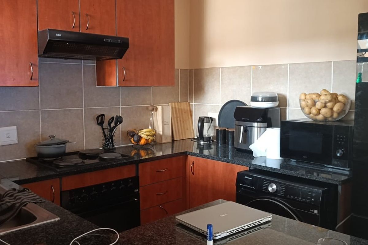 Functional kitchen featuring granite countertops, wooden cabinetry, built-in oven, electric hob, and tiled backsplash, offering a practical layout for daily meal preparation.