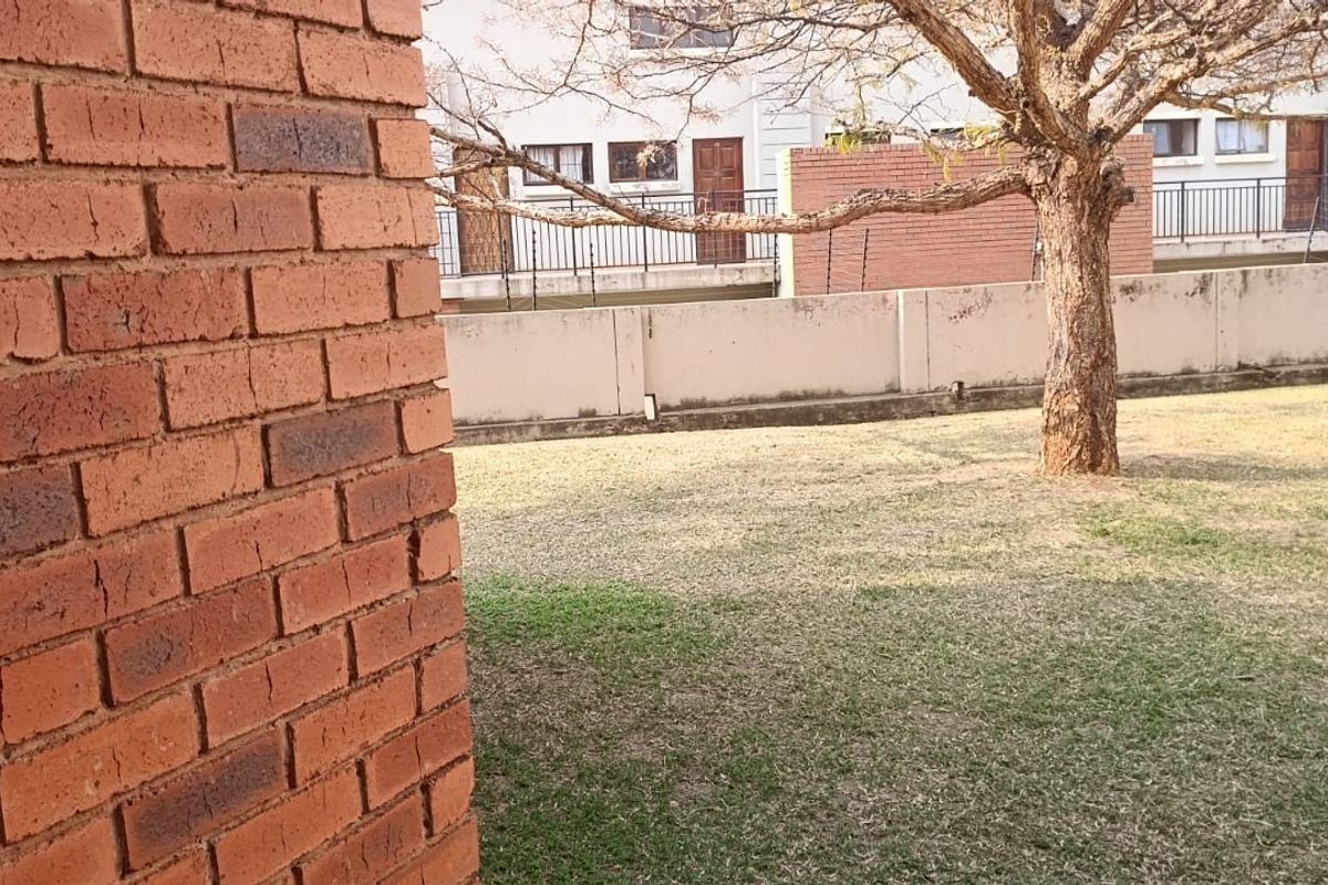 A view of the rear garden area featuring a brick wall and established lawn within the apartment complex grounds.