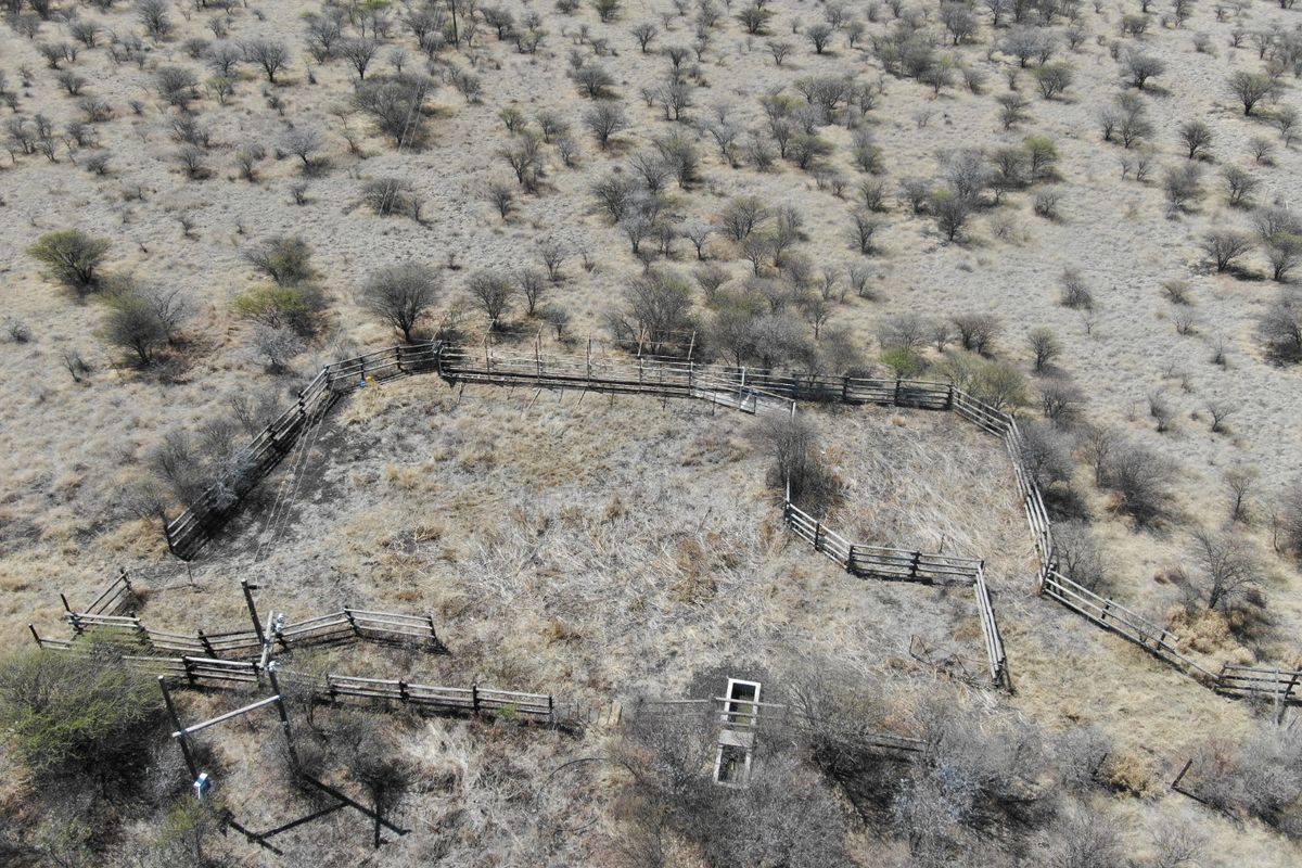 Aerial view of a vacant residential plot featuring livestock fencing, a concrete water trough, and an existing utility pole connection.