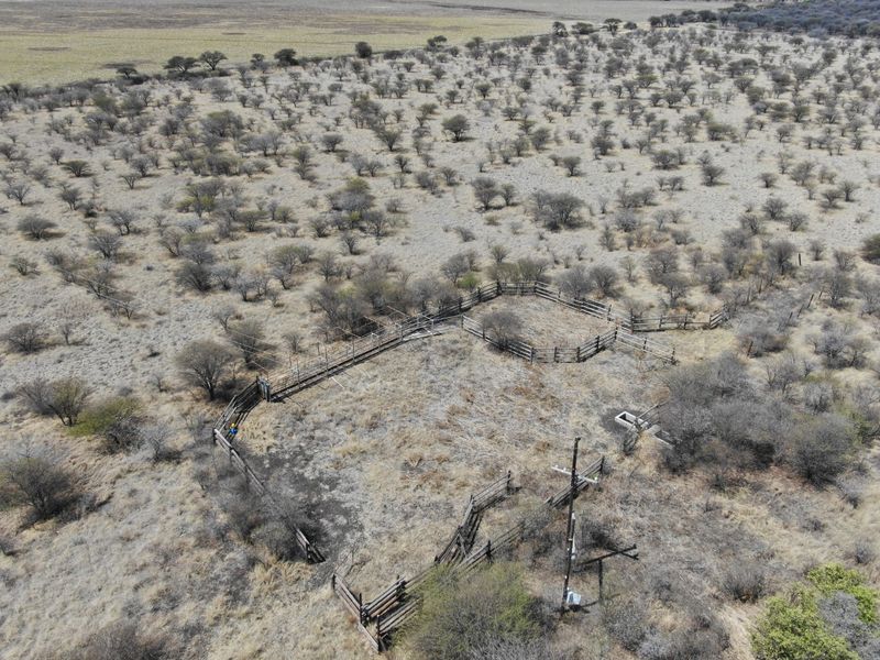 Aerial view of a rural property featuring a livestock enclosure, cattle kraal, utility pole, and water trough set within a natural landscape.