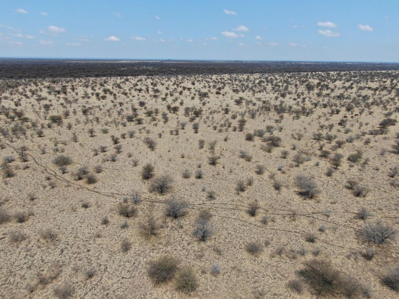 An aerial view of expansive, undeveloped residential land featuring native scrub vegetation and open terrain under a clear sky.