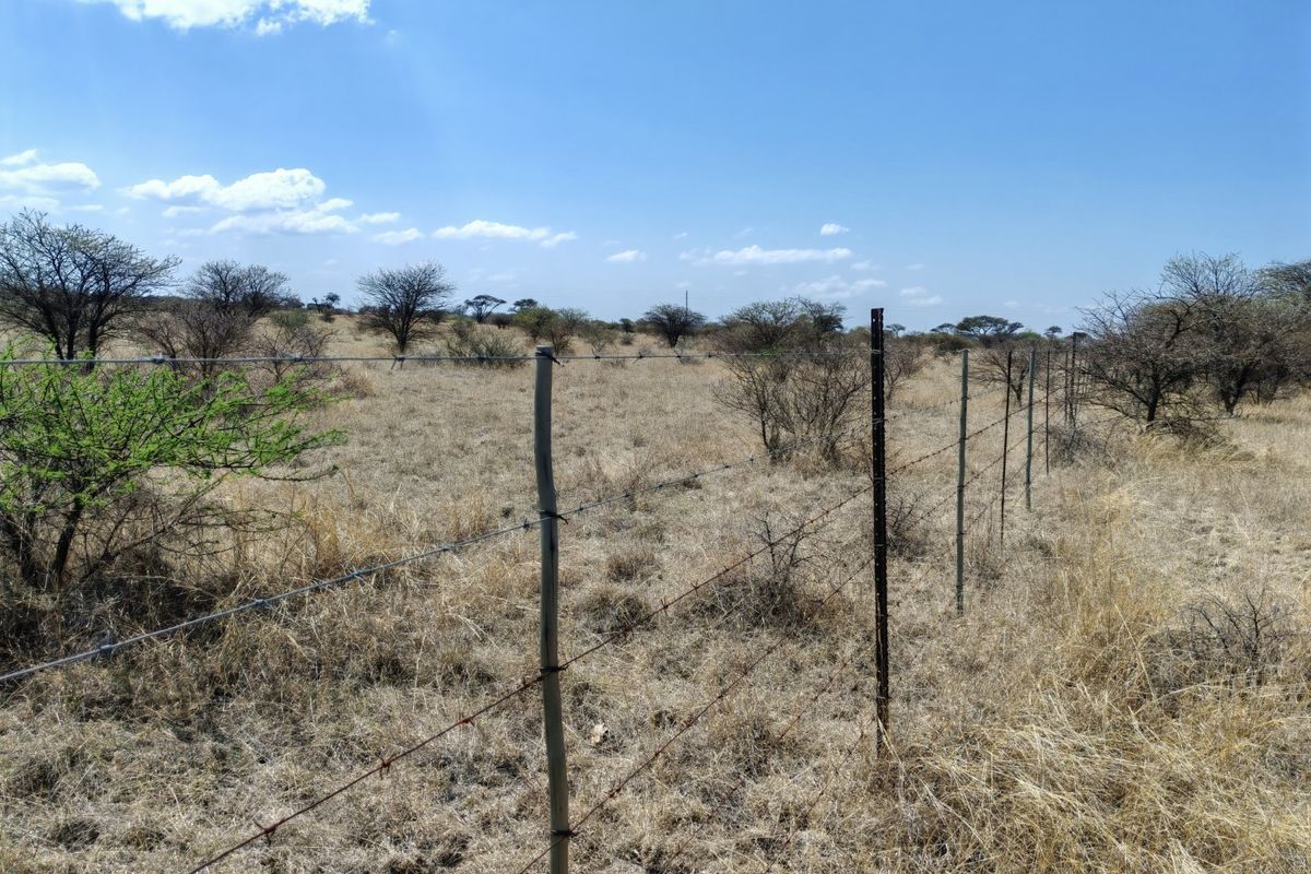 A view of a vacant residential plot featuring dry grassland, native shrubs, and perimeter barbed wire fencing with metal and wooden posts.