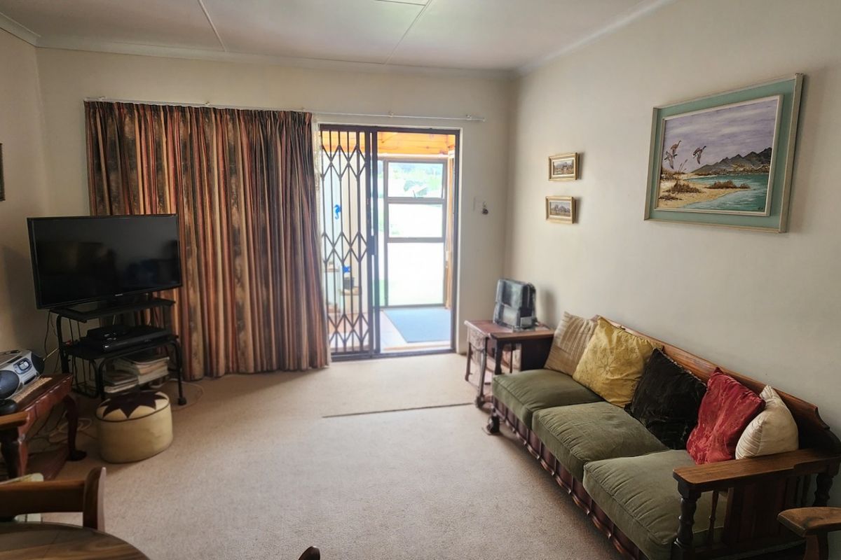 A living room featuring carpeted flooring, cove cornicing, and a sliding glass door with a security gate leading to an outdoor area.