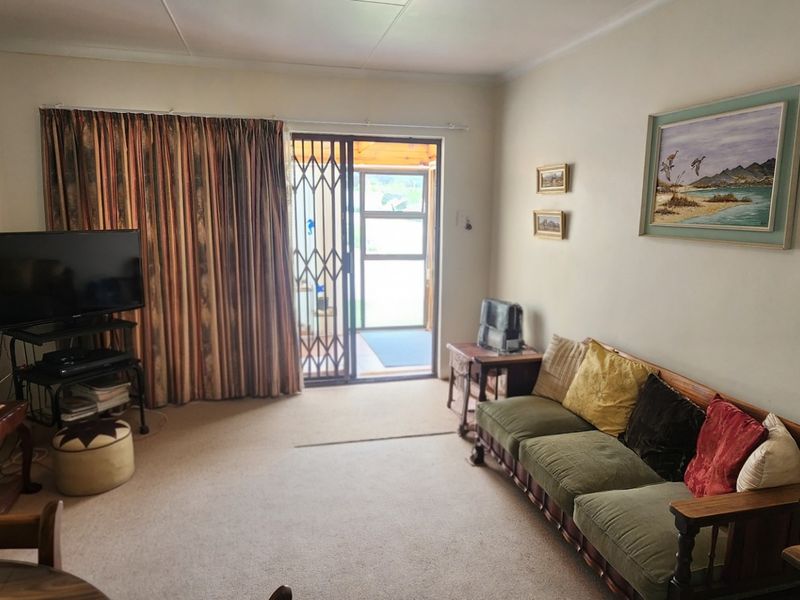 A living room featuring carpeted flooring, cove cornicing, and a sliding glass door with a security gate leading to an outdoor area.
