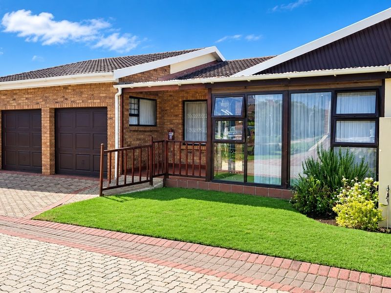 Front view of a well-maintained townhouse featuring a double garage, brick exterior, paved driveway, and a covered entrance with a small garden area.