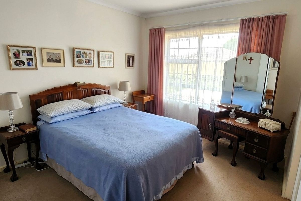 A carpeted bedroom featuring a window with security bars and built-in wardrobe storage.