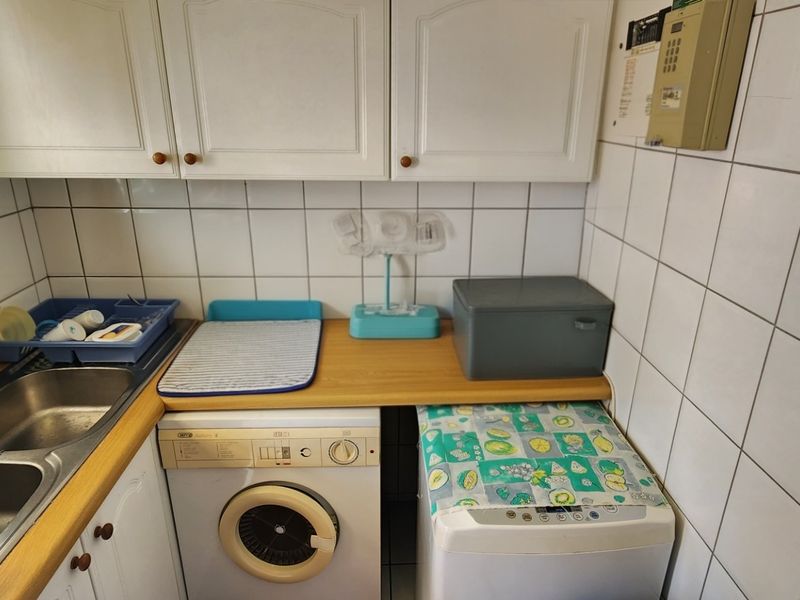 A functional laundry area featuring a double stainless steel sink, laminate countertop, and wall-mounted cabinetry with tiled splashbacks.