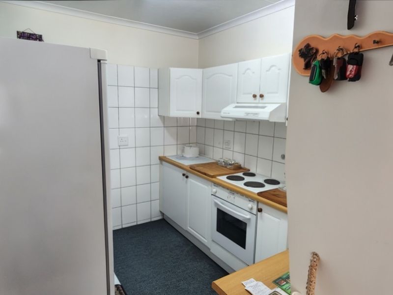 Compact kitchen featuring white cabinetry, built-in oven, electric hob, extractor fan, and tiled splashback.