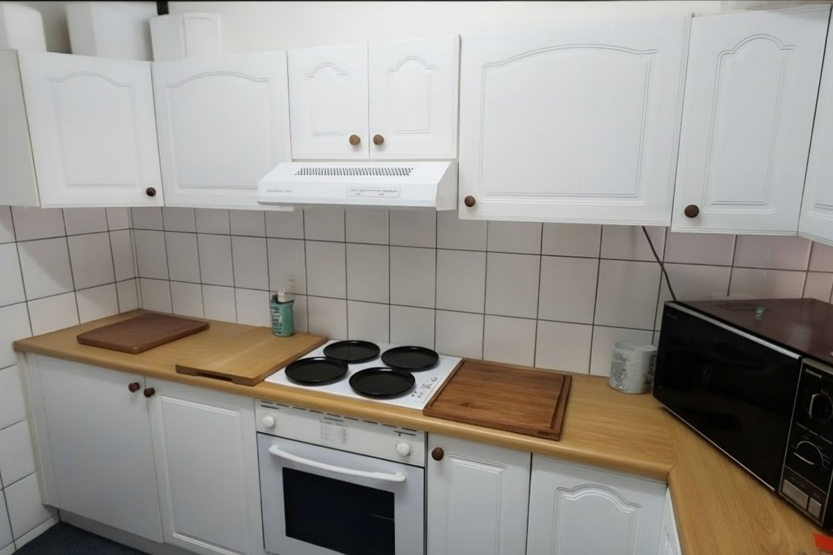 A functional kitchen featuring white cabinetry, laminate countertops, a tiled backsplash, and integrated cooking appliances including an oven and extractor fan.