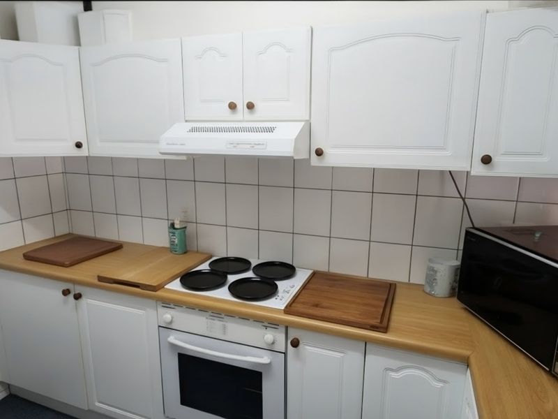 A functional kitchen featuring white cabinetry, laminate countertops, a tiled backsplash, and integrated cooking appliances including an oven and extractor fan.