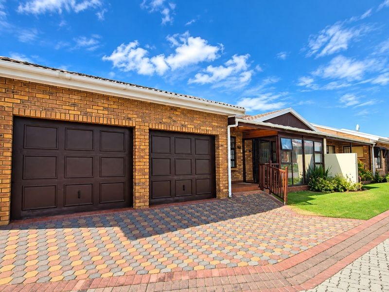 Front exterior view of a townhouse featuring a double garage, paved driveway, and an enclosed entrance porch with brick facade.