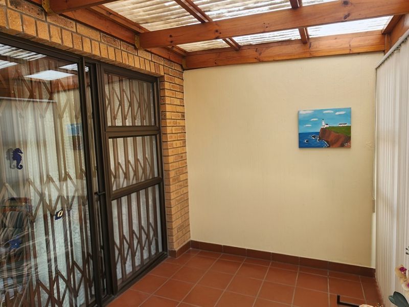 A covered patio area featuring a timber pergola, translucent roof, brick walling, and tiled flooring, providing a functional outdoor space.
